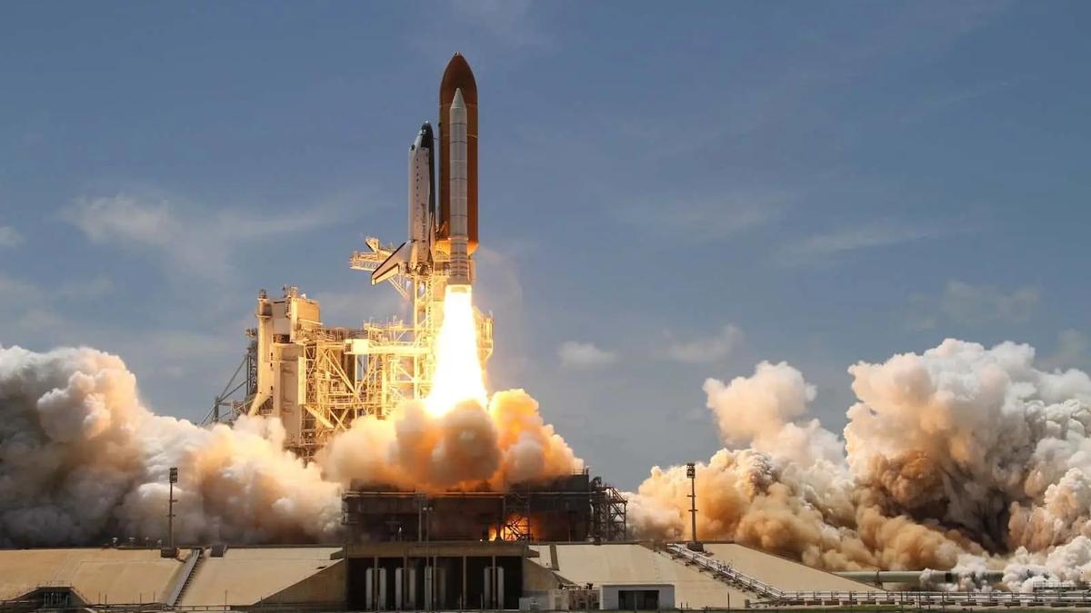 A space shuttle launching from a pad, engulfed in flames and billowing smoke