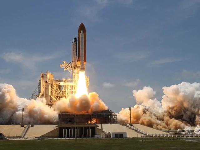 A space shuttle launching from a pad, engulfed in flames and billowing smoke