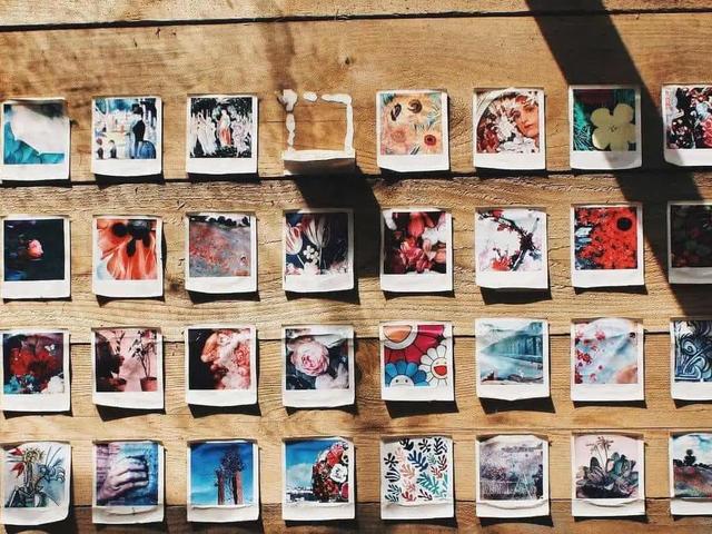 Una cuadrícula de fotos Polaroid de colores, colocadas con chinchetas en una pared de madera, dispuestas en filas