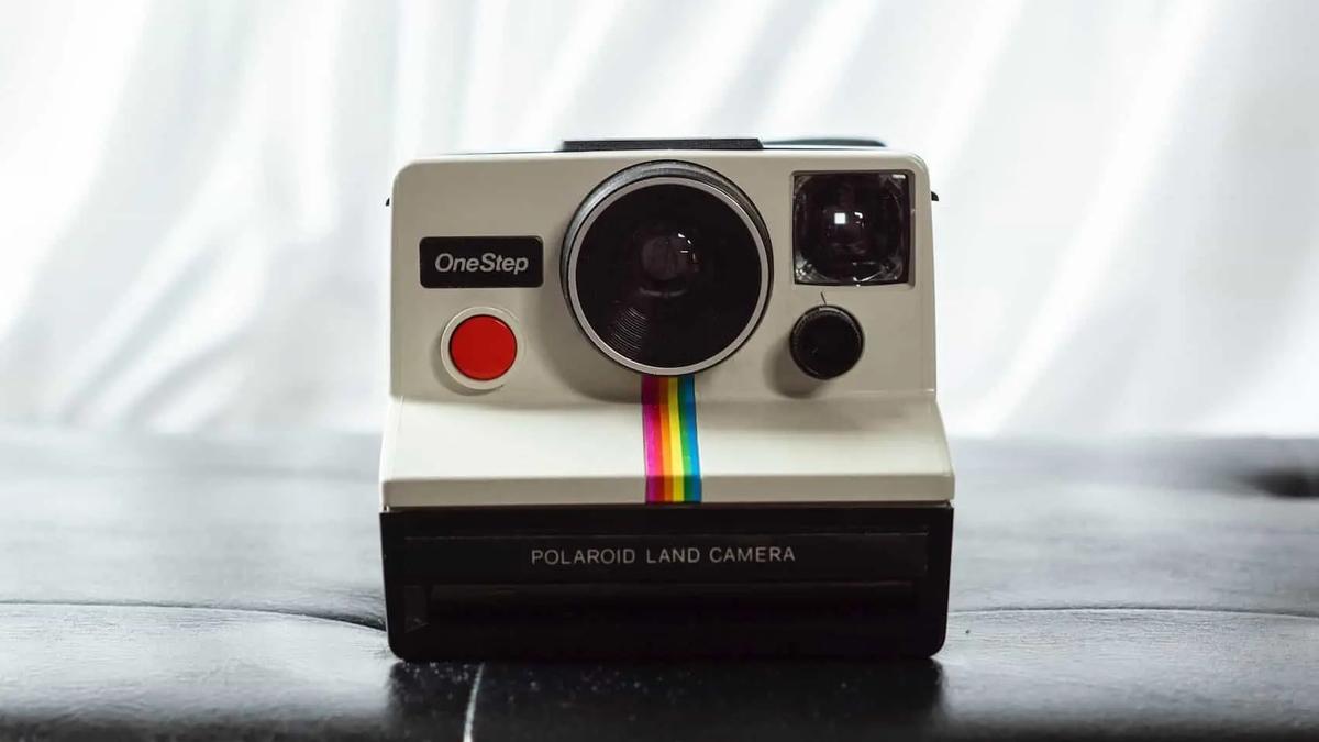 A vintage Polaroid OneStep Land Camera with a rainbow stripe, sitting on a dark surface