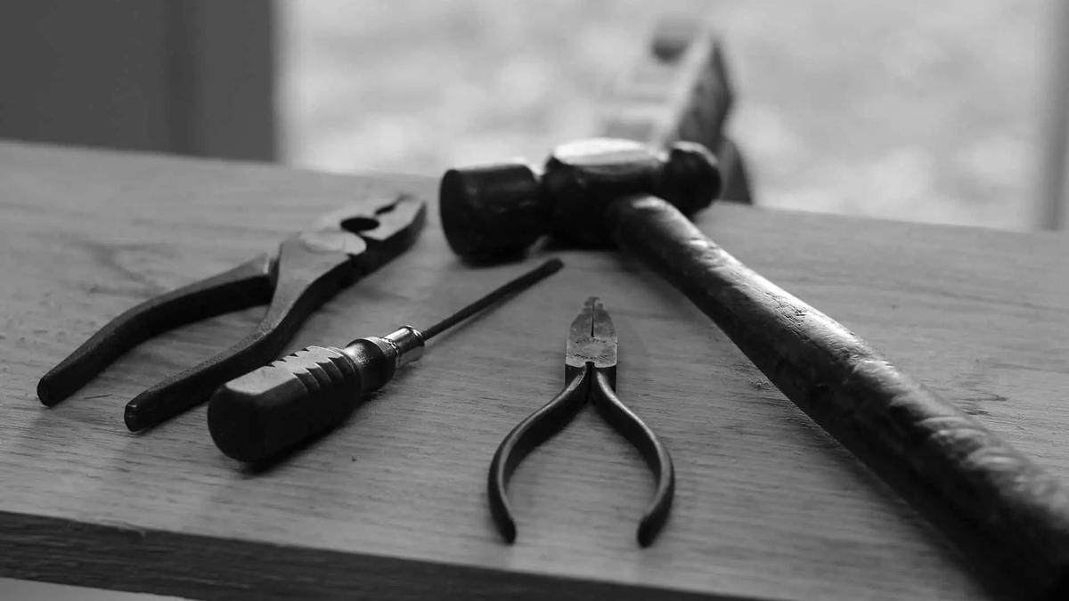 Black and white photo of pliers, a screwdriver and a hammer laid on a wooden workbench