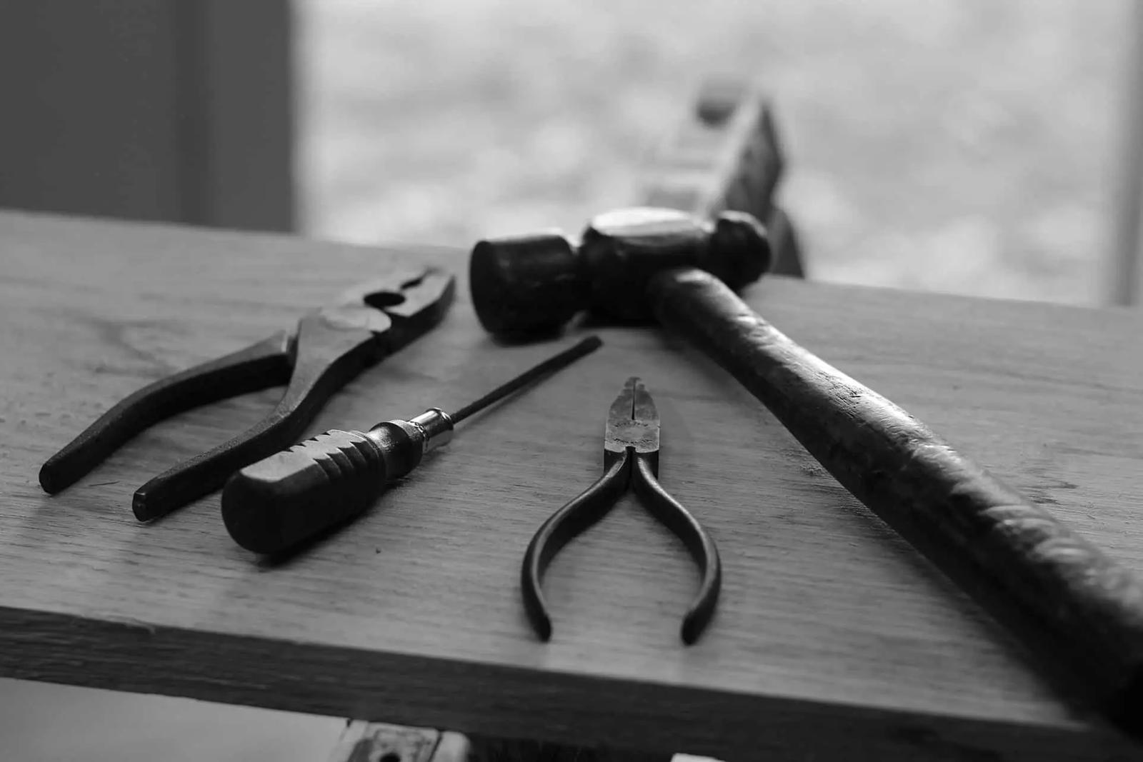 Foto en blanco y negro de unos alicates, un destornillador y un martillo sobre una mesa de madera