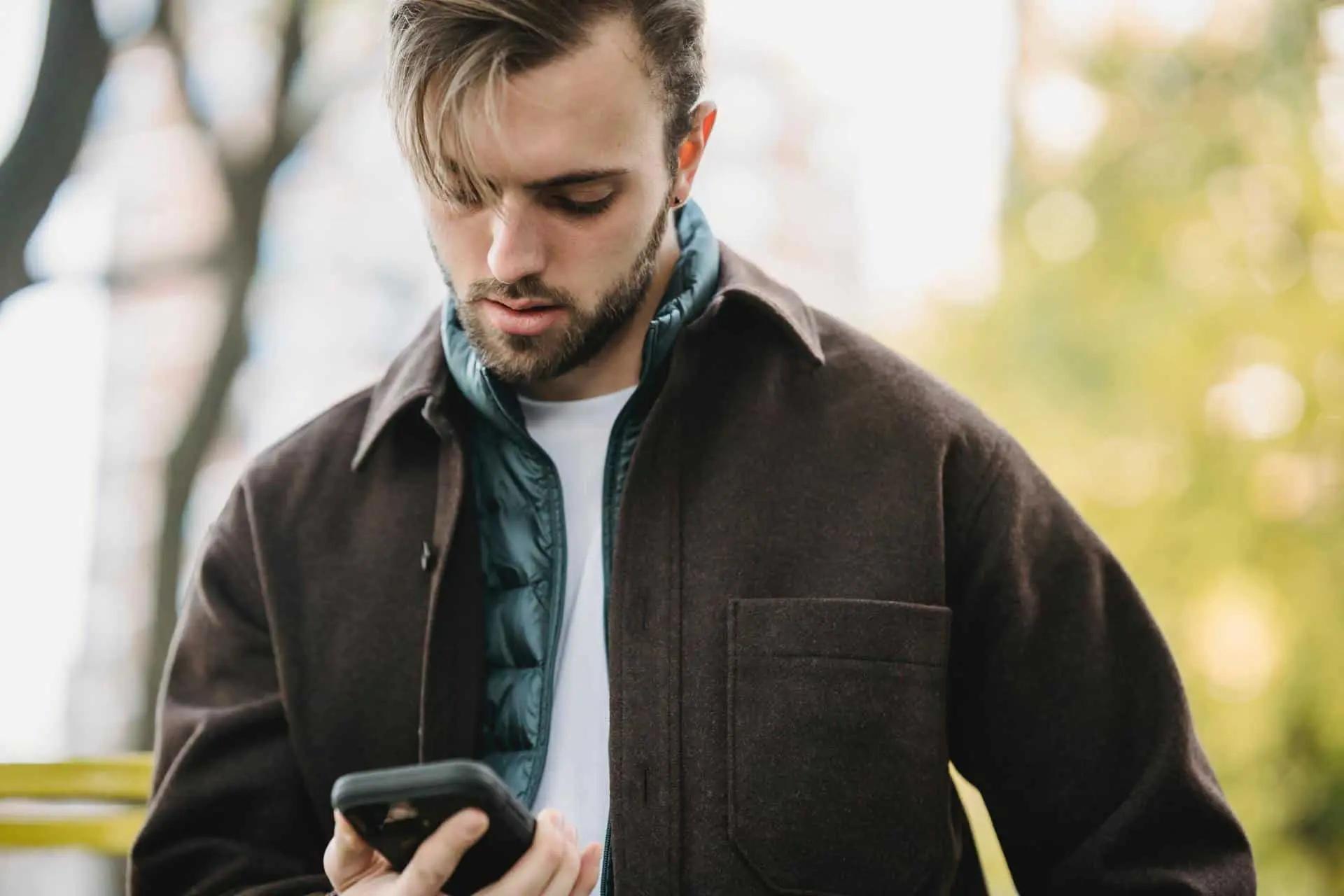 A man in a jacket looking down at his phone while standing outdoors