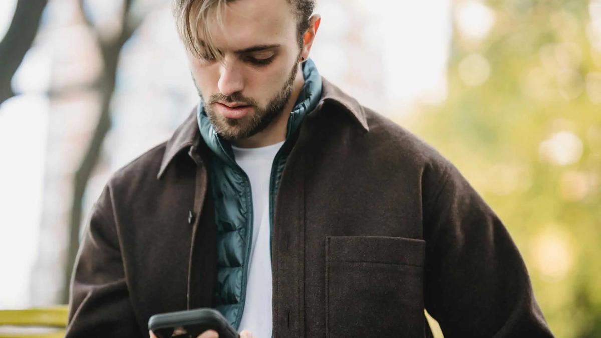 Un hombre con chaqueta mirando el teléfono mientras está de pie al aire libre