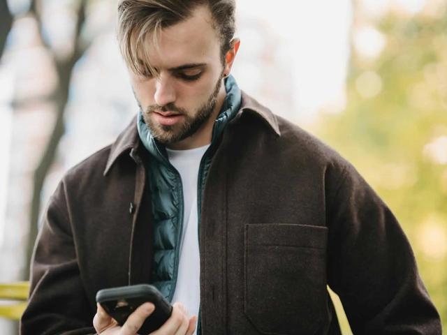 Un hombre con chaqueta mirando el teléfono mientras está de pie al aire libre
