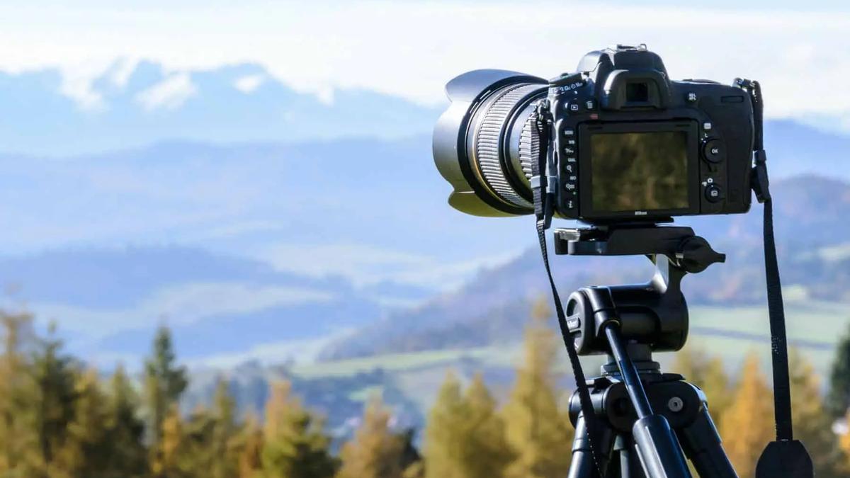 A DSLR camera on a tripod overlooking a mountain valley with forested hills.