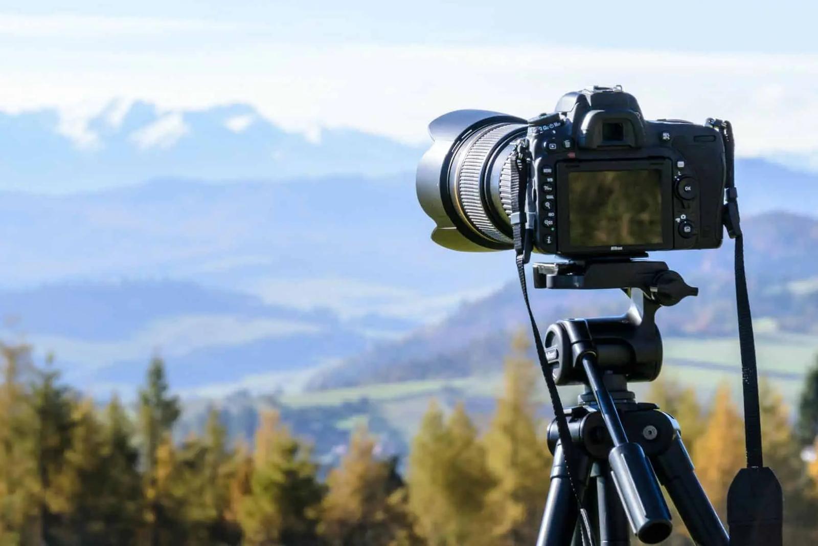 A DSLR camera on a tripod overlooking a mountain valley with forested hills.