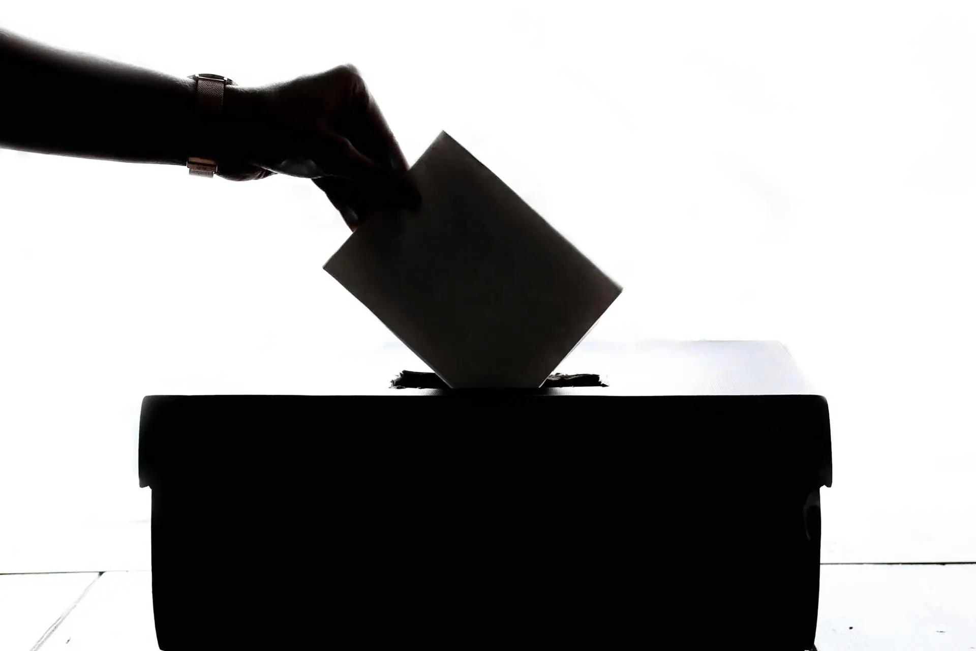 Silhouette of a hand placing a paper ballot into a box slot