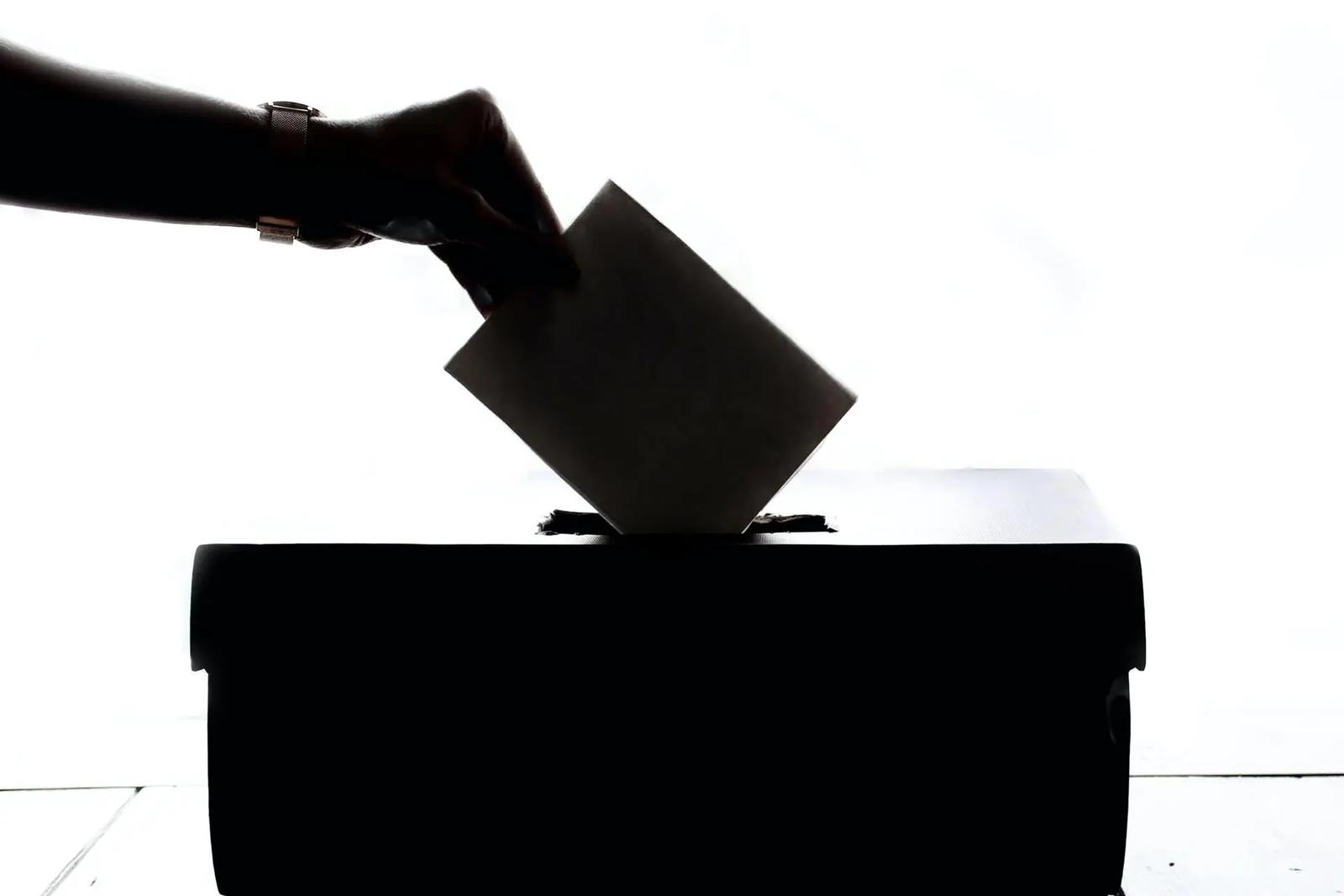 Silhouette of a hand placing a paper ballot into a box slot