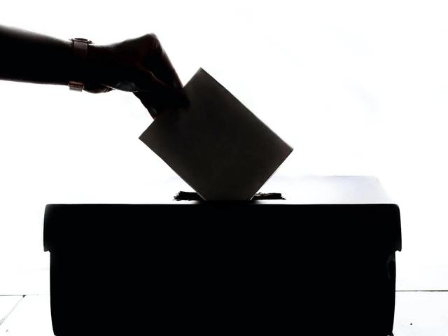 Silhouette of a hand placing a paper ballot into a box slot