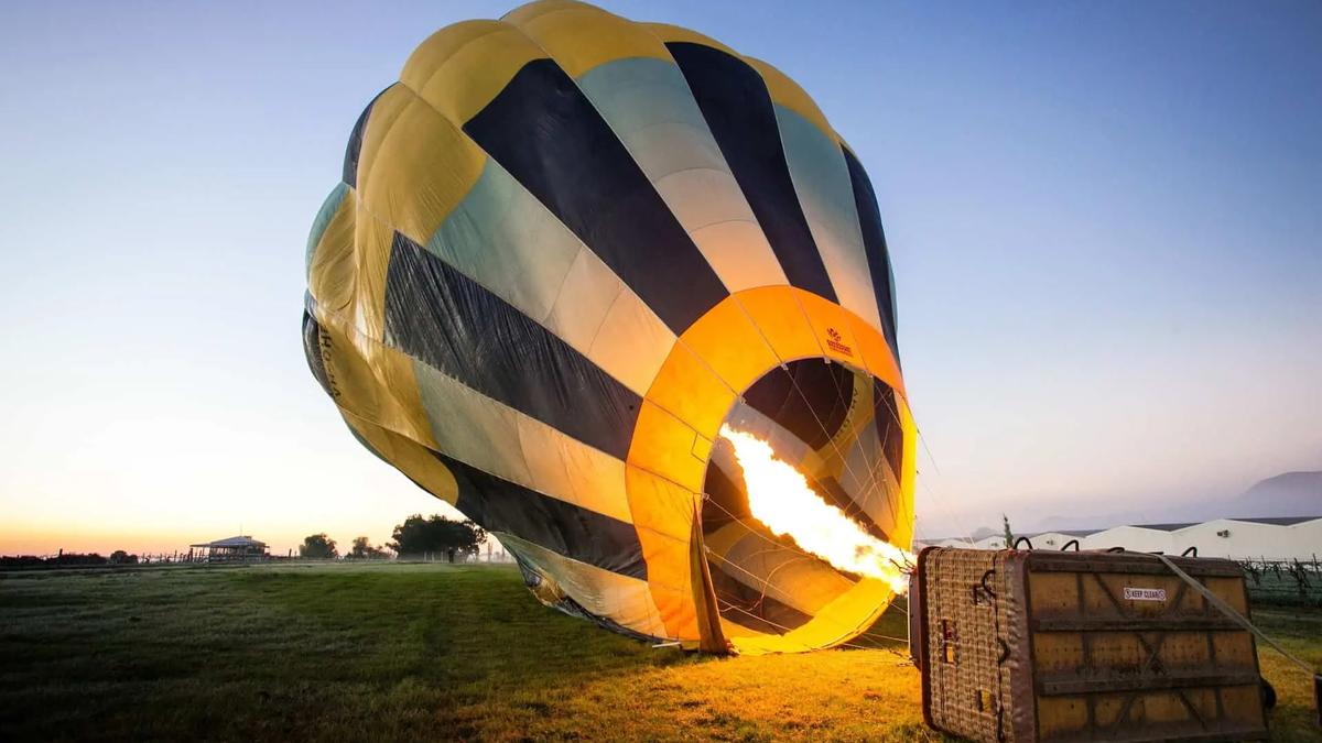 A hot air balloon being inflated with a burner flame in an open field at dawn