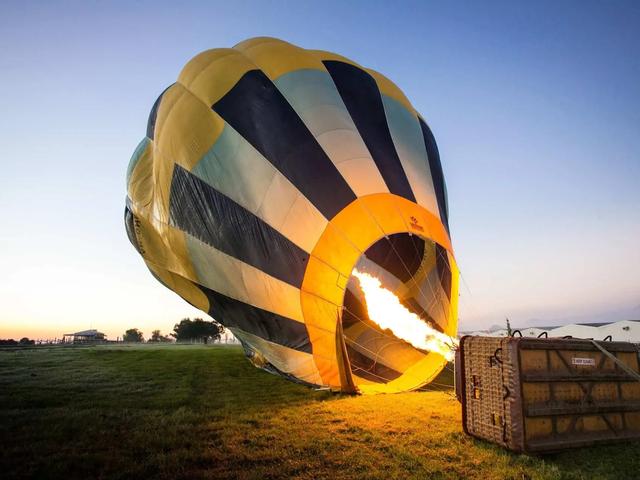 A hot air balloon being inflated with a burner flame in an open field at dawn