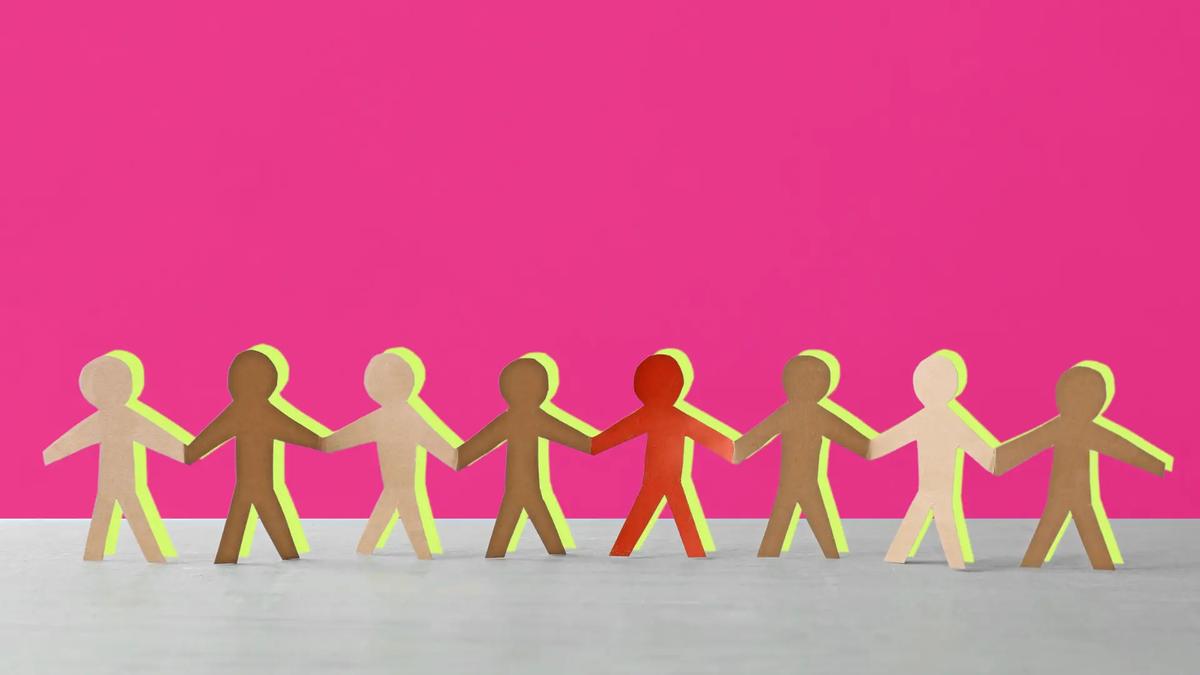 Nine paper cutouts of people in varying skin tones, holding hands, against a bright pink background