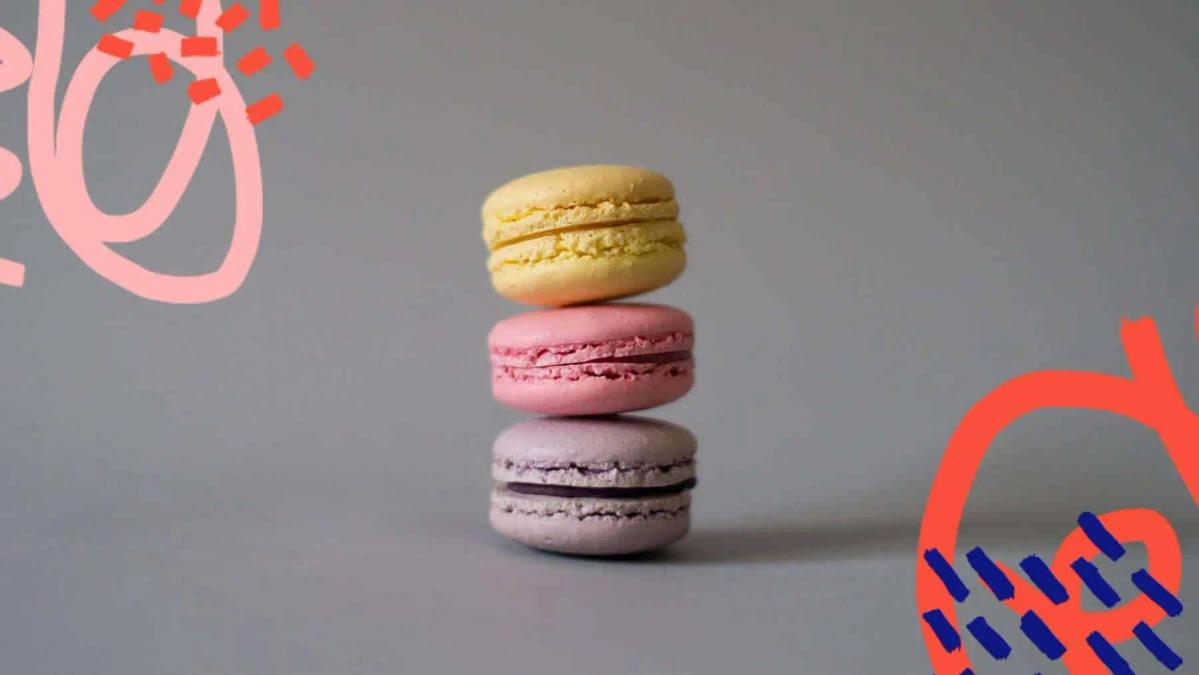 Three stacked macarons in yellow, pink and purple on a grey background with red graphic accents