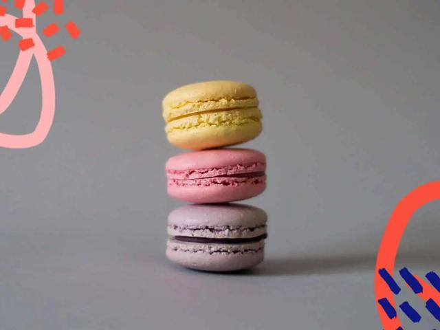 Tres macarons apilados en amarillo, rosa y morado sobre fondo gris con acentos gráficos rojos