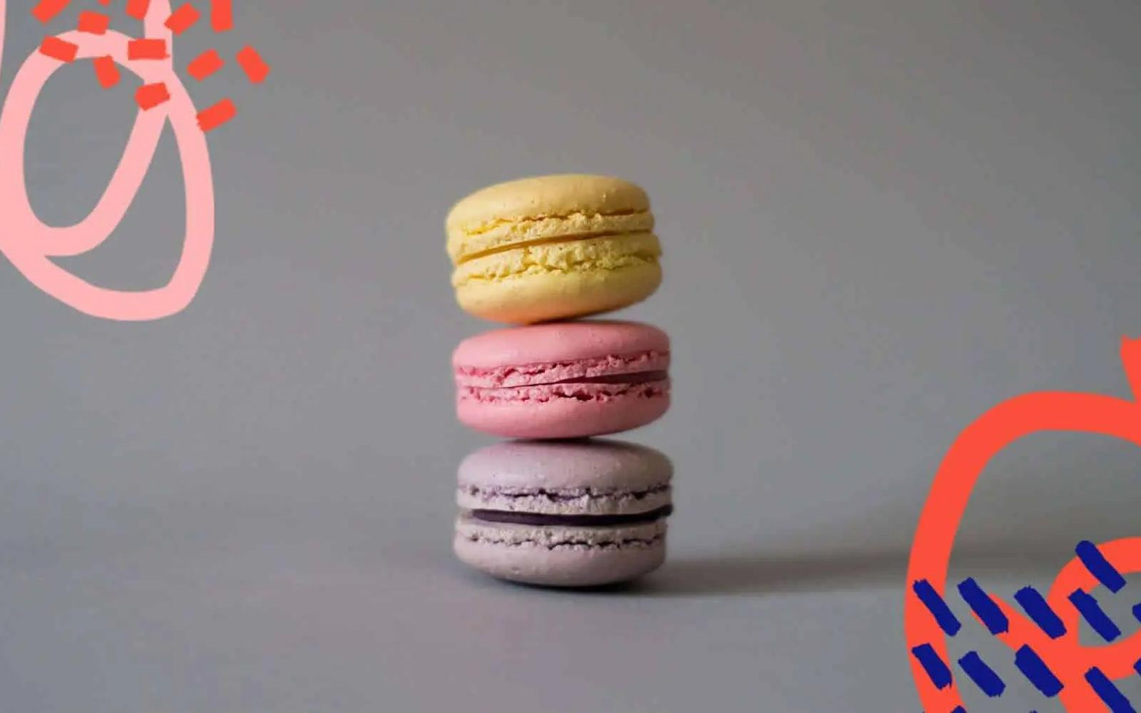 Three stacked macarons in yellow, pink and purple on a grey background with red graphic accents