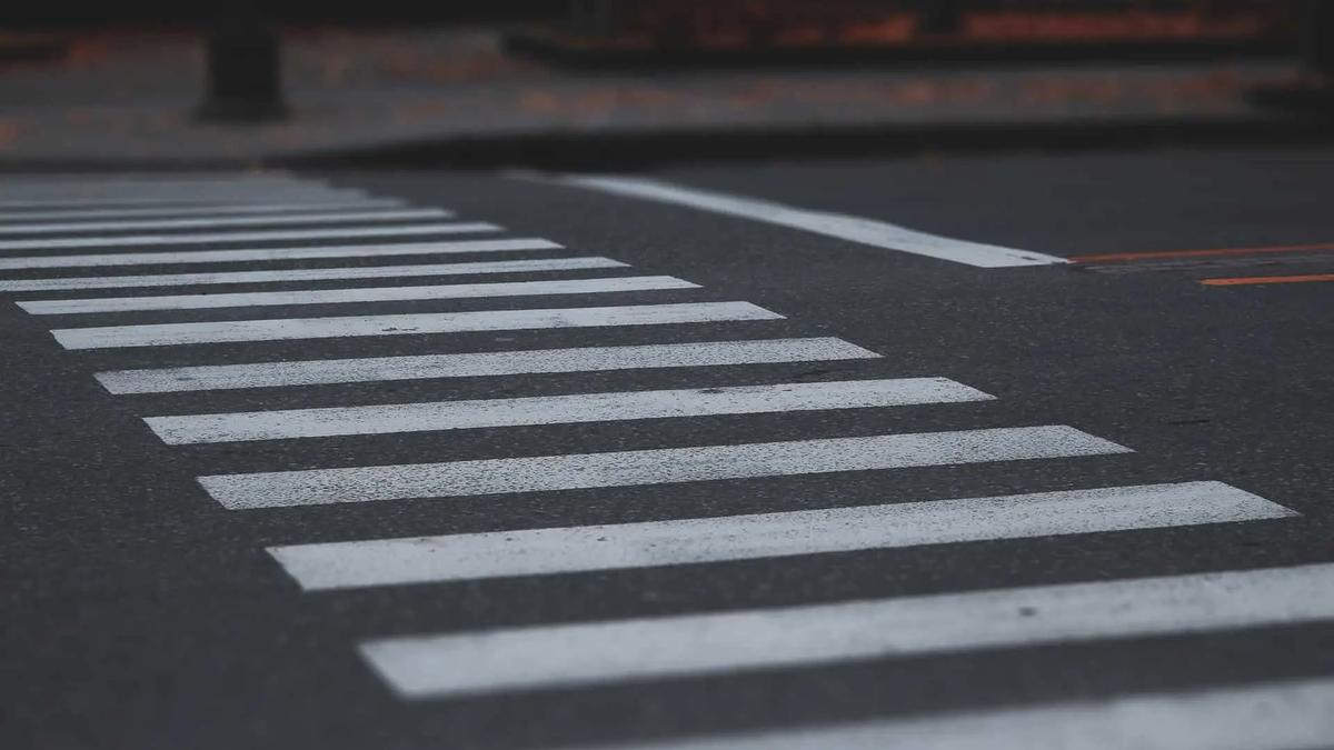 Dark asphalt road with a white crosswalk and a white line on the right, orange lines visible in the distance