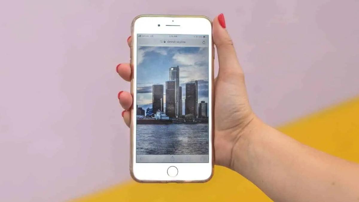 A hand holding a phone displaying a photo of a city skyline along a waterfront