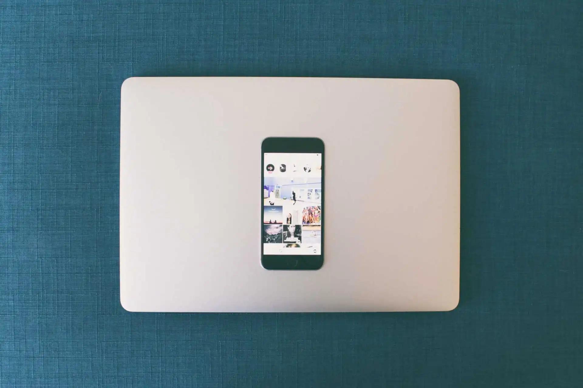 A smartphone showing an Instagram grid of photos, resting on a closed laptop