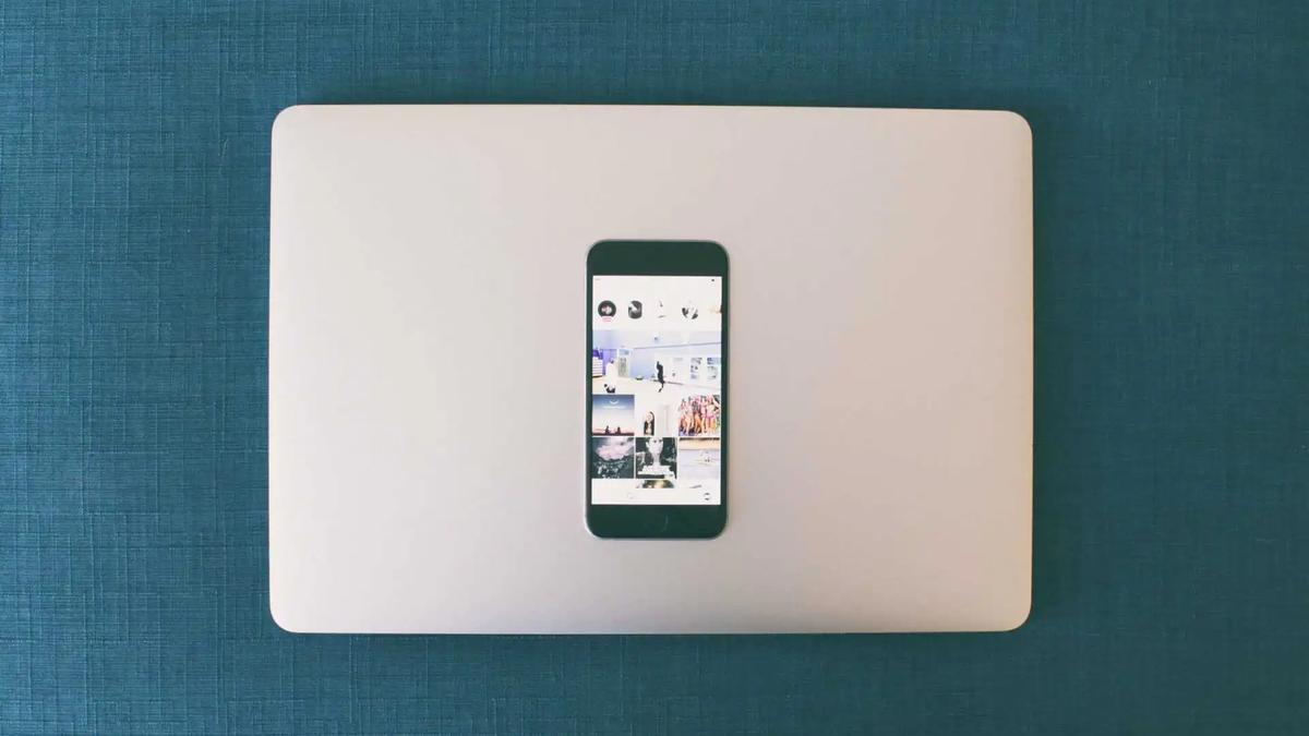 A smartphone showing an Instagram grid of photos, resting on a closed laptop