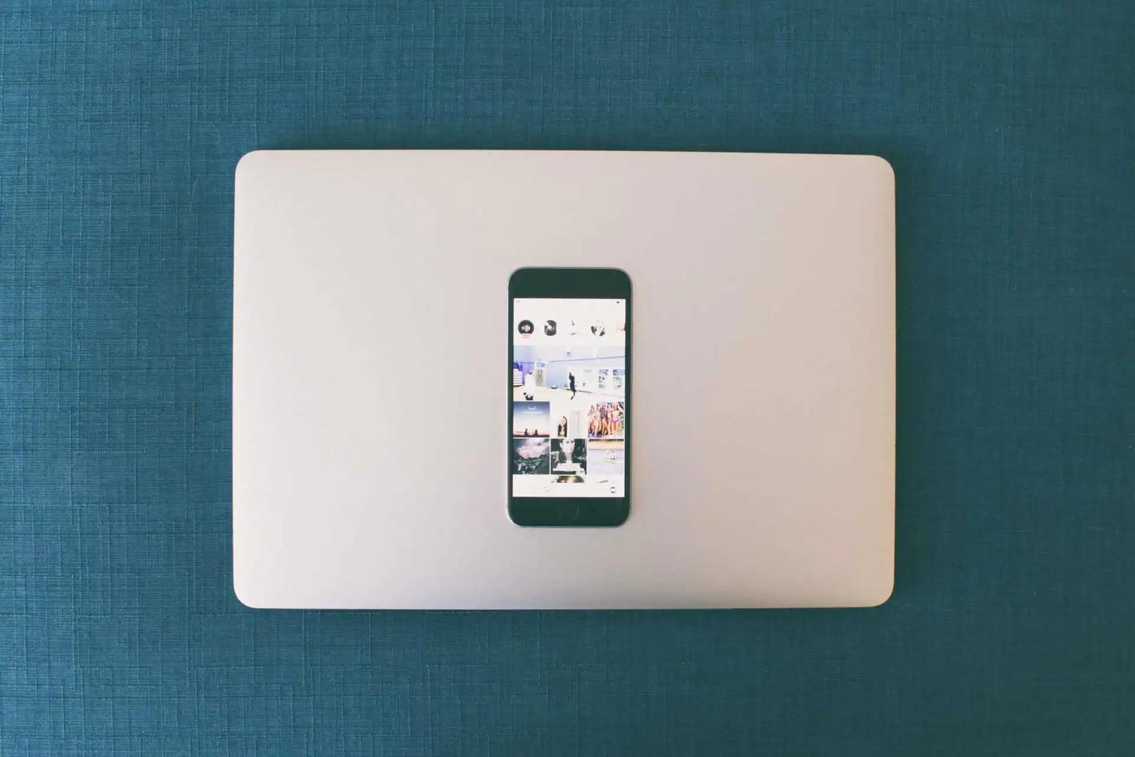 Un smartphone con una cuadrícula de fotos de Instagram, apoyado sobre una laptop cerrada