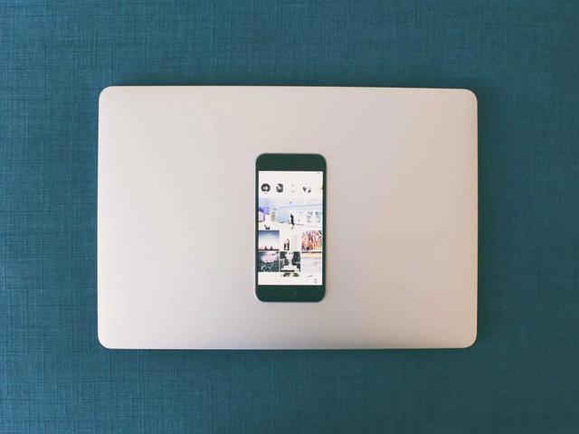 Un smartphone con una cuadrícula de fotos de Instagram, apoyado sobre una laptop cerrada