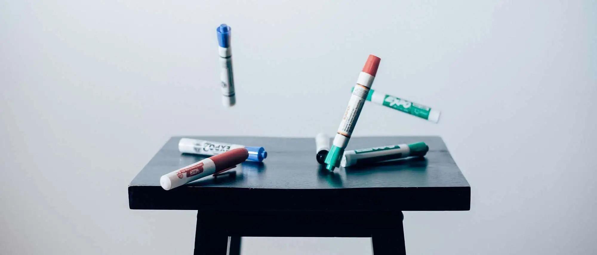 Colored markers scattered on and floating above a small black stool