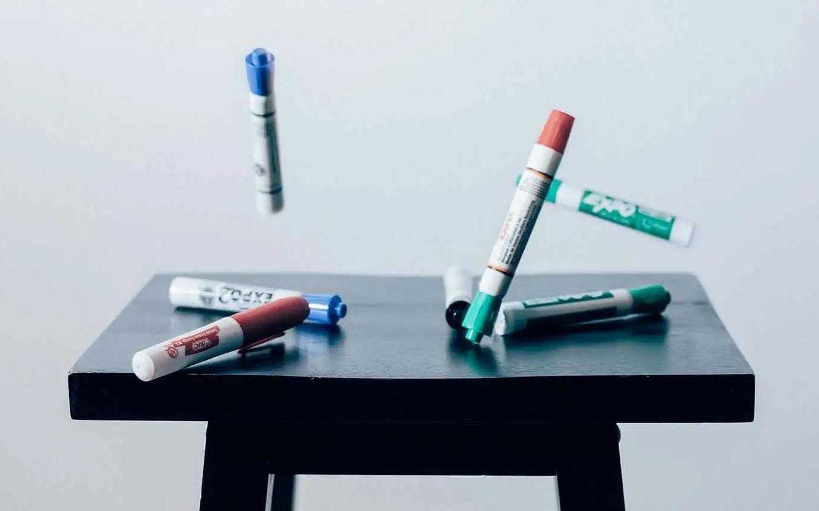 Colored markers scattered on and floating above a small black stool