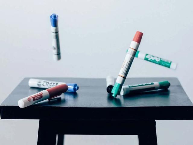 Colored markers scattered on and floating above a small black stool
