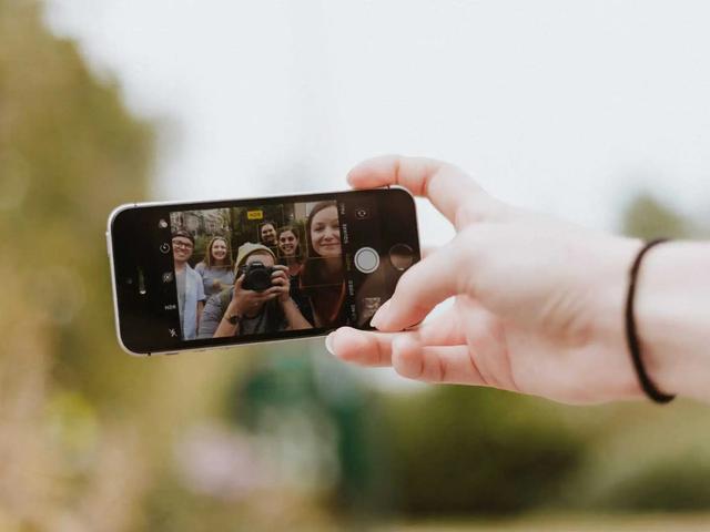 Una mano sostiene un telefono fotografiando a un grupo de amigos posando al aire libre