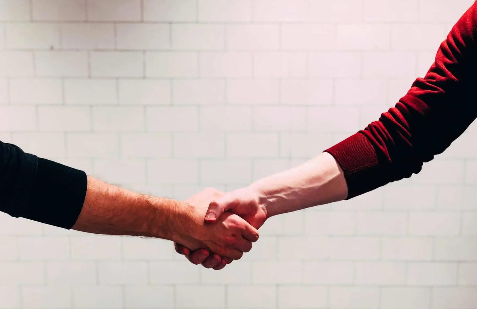 Two people shaking hands in front of a white tiled wall