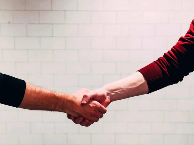 Two people shaking hands in front of a white tiled wall
