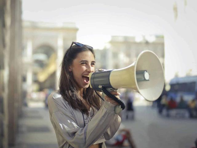 A woman shouts into a large megaphone on an outdoor city street