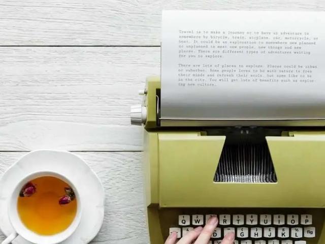 Manos escribiendo en una máquina de escribir vintage junto a una taza de té y flores rosas sobre una mesa de madera