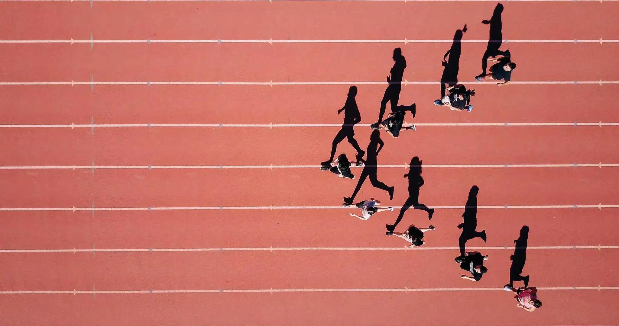 Aerial view of runners racing on a red athletics track, casting long shadows