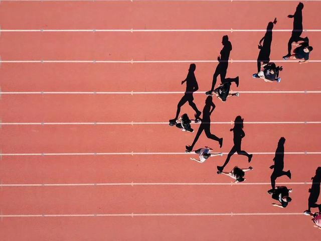 Aerial view of runners racing on a red athletics track, casting long shadows