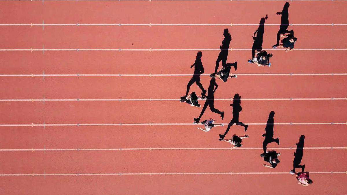 Aerial view of runners racing on a red athletics track, casting long shadows