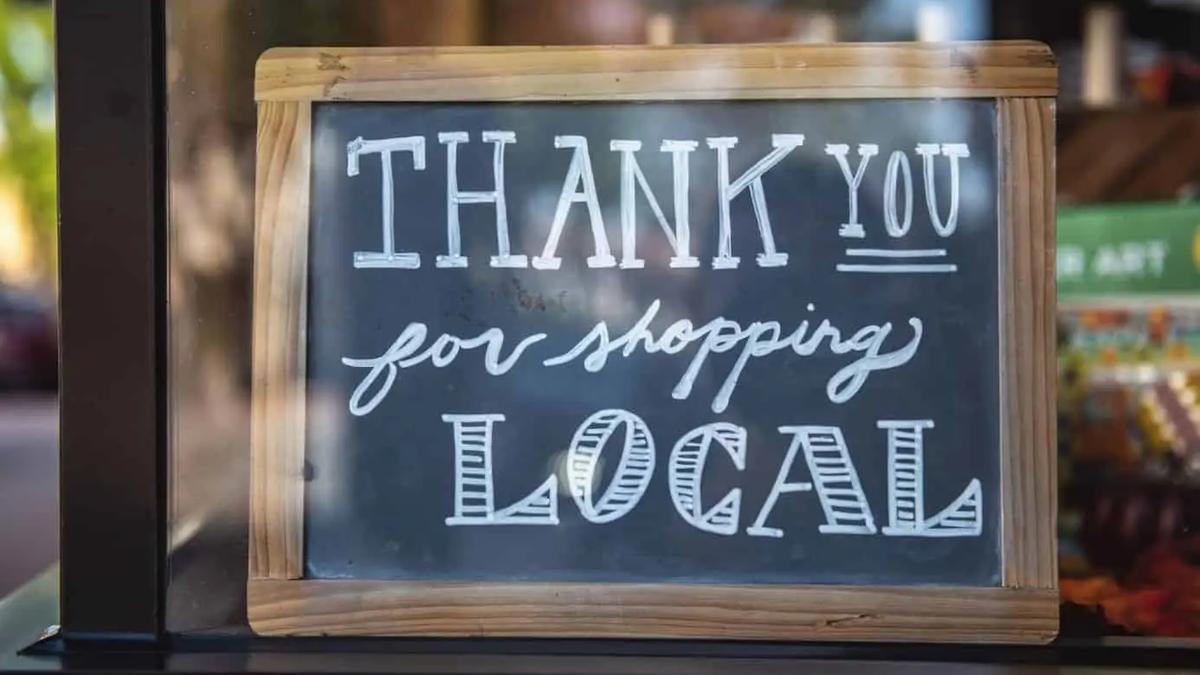 A wooden-framed chalkboard sign in a shop window reading "Thank you for shopping local"