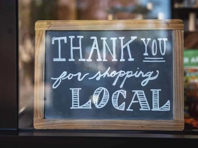 A wooden-framed chalkboard sign in a shop window reading "Thank you for shopping local"