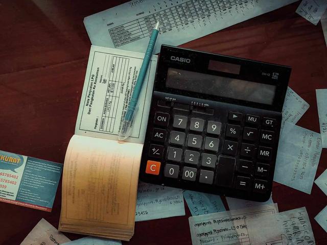 A calculator, receipt book, pen and handwritten notes scattered on a desk