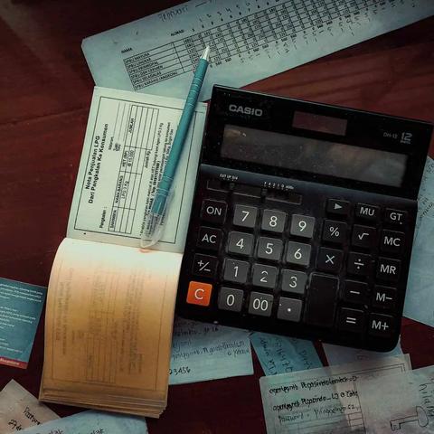 A calculator, receipt book, pen and handwritten notes scattered on a desk