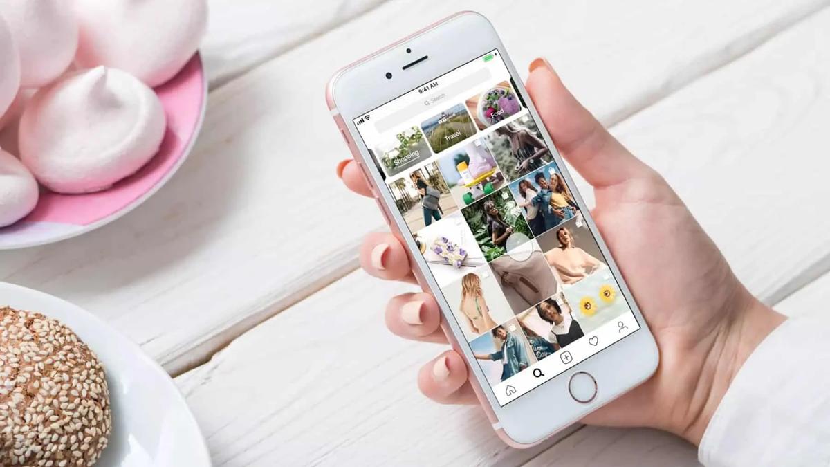 A hand holds a phone showing the Instagram explore grid with shopping and travel category tags