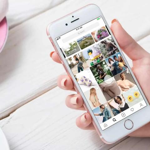 A hand holds a phone showing the Instagram explore grid with shopping and travel category tags