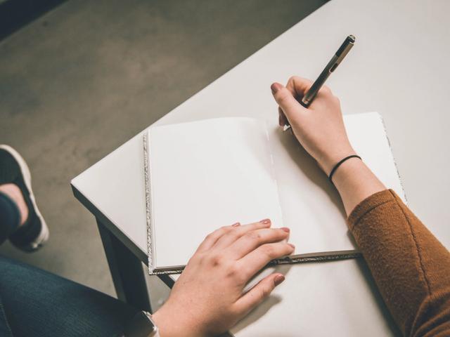 Overhead view of a person writing in a blank notebook on a desk