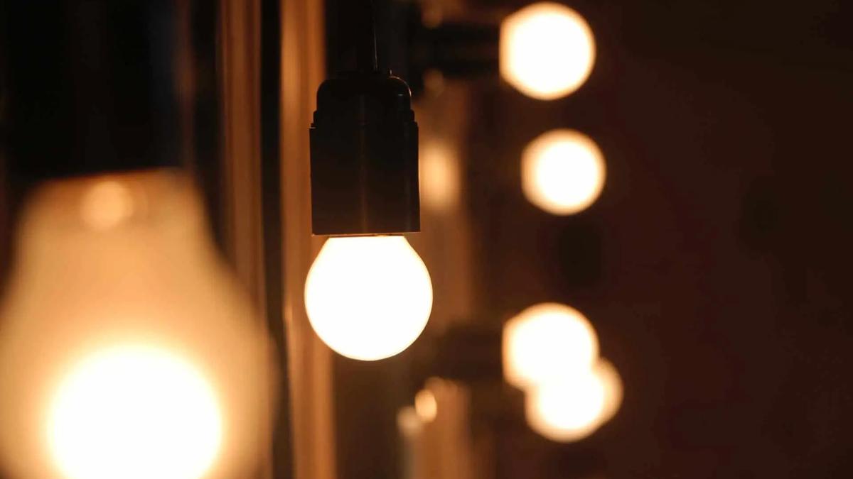 Row of bright, warm white light bulbs on a dark background, with one bulb in focus in the foreground