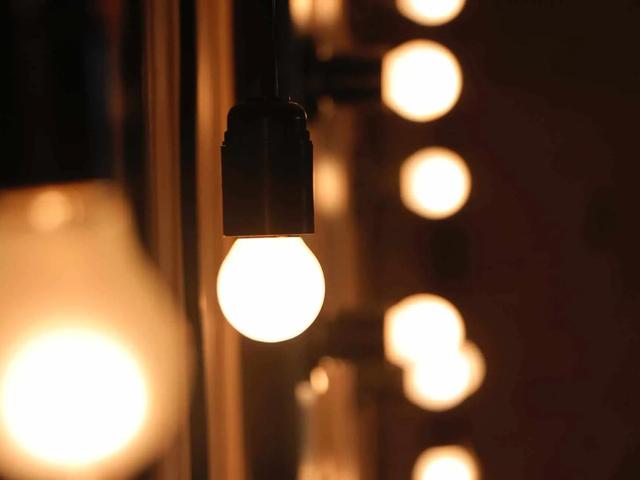 Row of bright, warm white light bulbs on a dark background, with one bulb in focus in the foreground