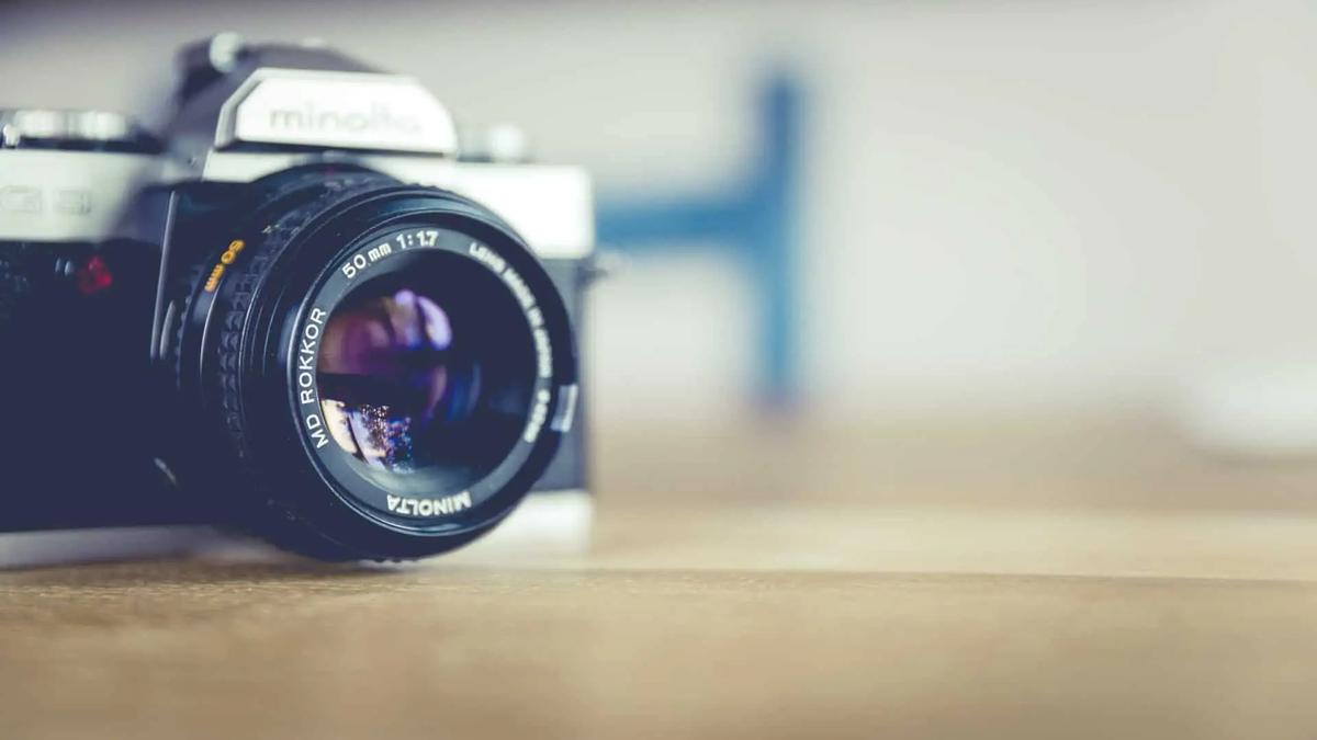 A vintage Minolta film camera with a 50mm lens resting on a wooden surface