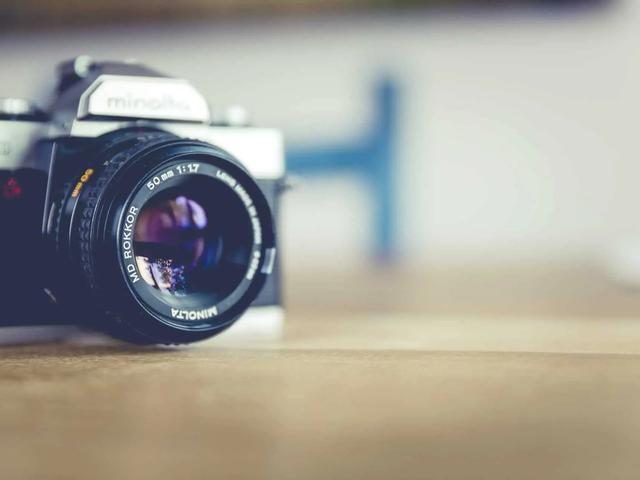 A vintage Minolta film camera with a 50mm lens resting on a wooden surface