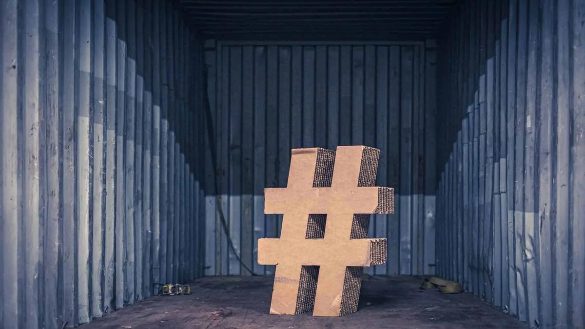Cardboard hashtag symbol in a dark, empty shipping container. Blue-grey walls, brown floor. Somber mood.