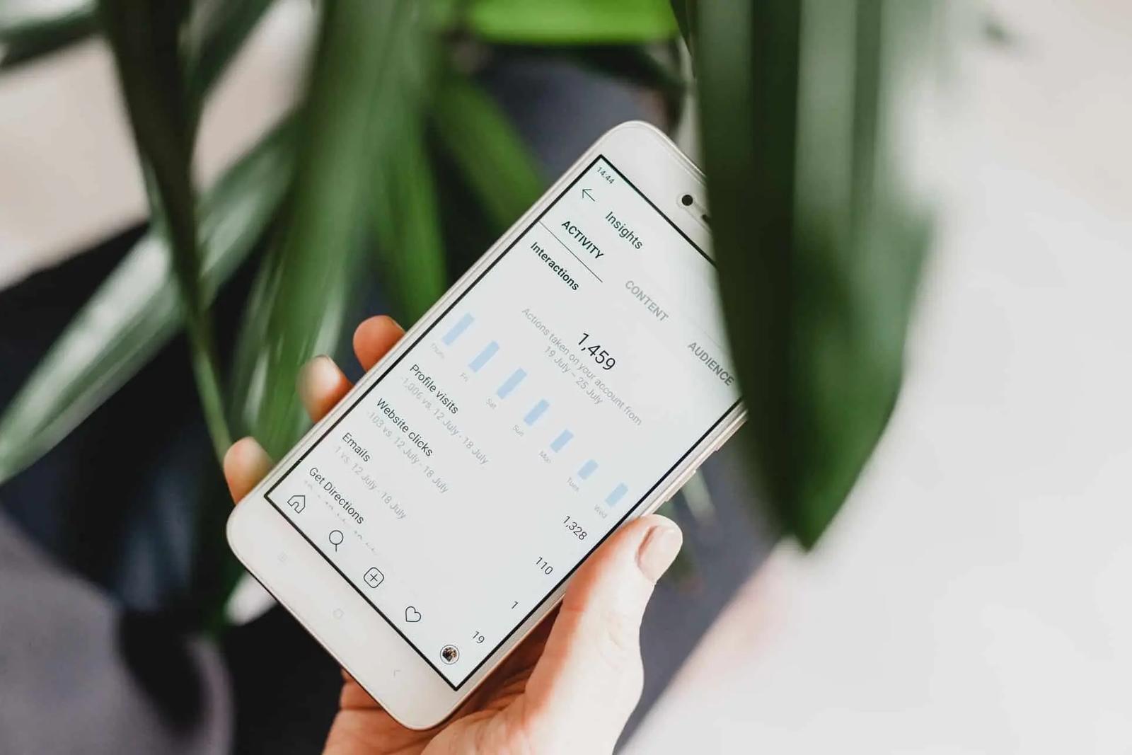 A hand holds a phone showing Instagram Insights, with a bar chart and profile visit stats